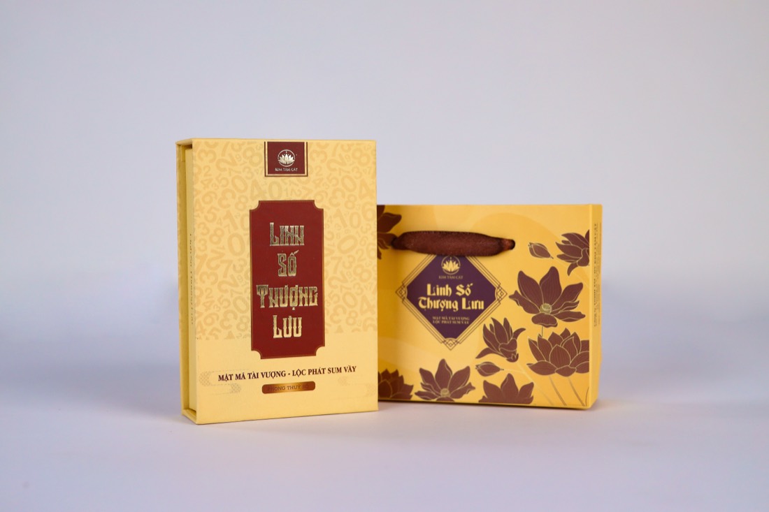 Hộp sim giấy vàng kem in Linh Số Thượng Lưu - Mật Mã Tài Vượng - Lộc Phát Sum Vầy đứng cạnh túi quà giấy màu vàng in hoa sen nâu, chụp trên nền trắng