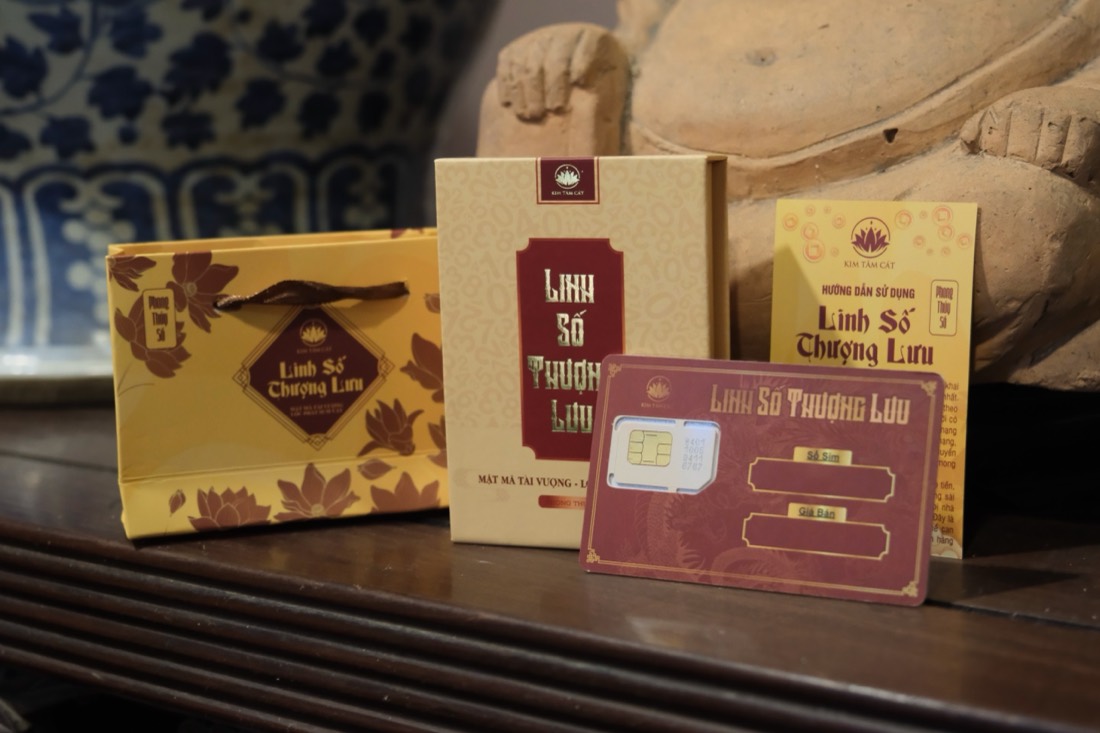 Bộ Linh Số Thượng Lưu bày trên mặt bàn gỗ gồm túi quà in hoa sen, hộp sim, thẻ Linh Số đỏ gắn phôi sim với ô trống Số Sim và Giá Bán, cùng tờ hướng dẫn sử dụng; phía sau là tượng gốm và lọ sứ hoa xanh