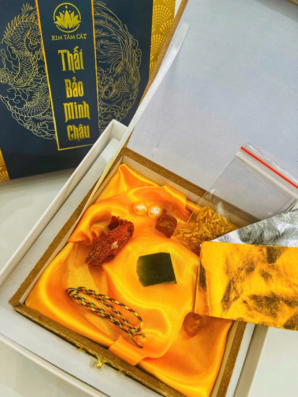 Hộp Thất Bảo Minh Châu mở nắp, các báu vật xếp trên tấm lụa vàng cùng lá vàng bạc và túi gạo